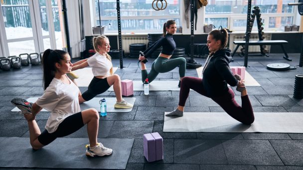 Strong young women stretching their hips and leg muscles while exercising on fitness mats indoors