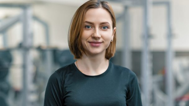 Portrait of young smiling woman in the gym, female fitness instructor looking at the camera.