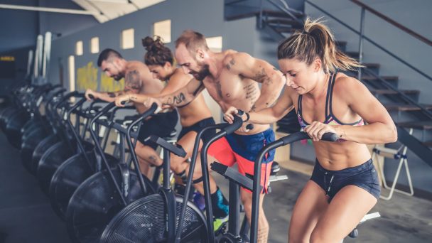 Four people training indoor gym using stationary bike - teammates, sportive, athletes concept