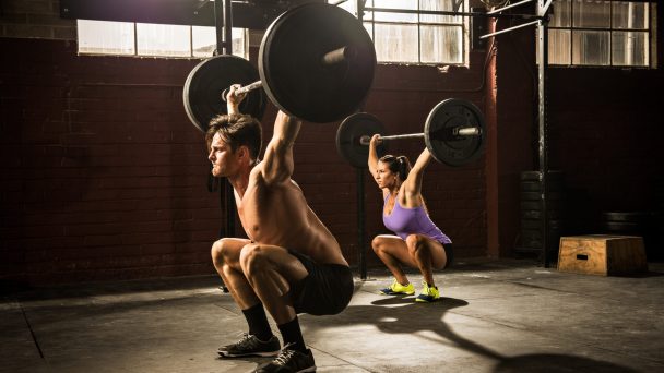 Two young adults lifting barbells in gym