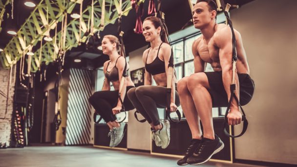 Beautiful young sports people are working out with TRX in gym